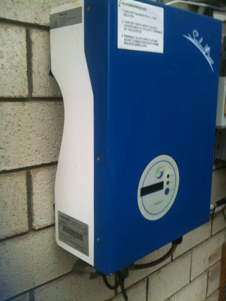 A blue solar inverter mounted on an outside brick wall